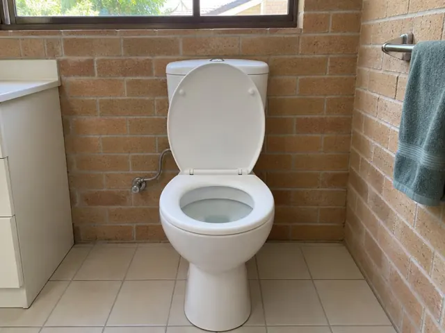 Clean white toilet in a tiled bathroom with brick-pattern wall and tiled floor in Forestville