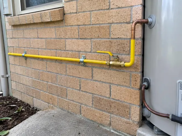 Exterior brick wall with yellow gas pipe, valve and copper fittings beside a house unit in Davidson