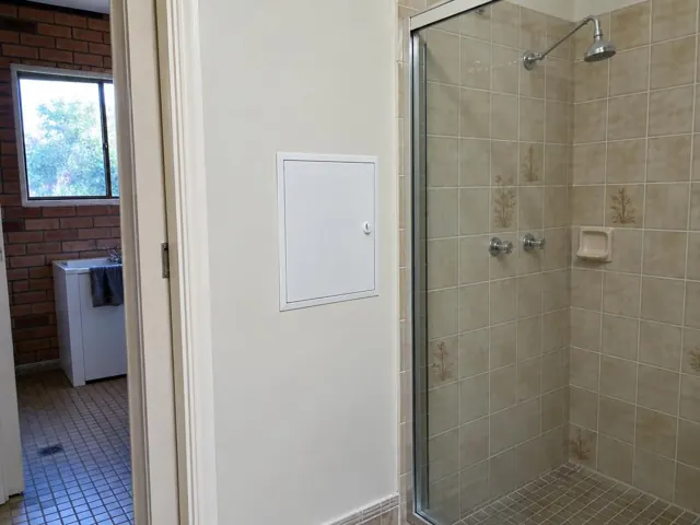 Small access panel in a tiled bathroom wall beside a shower in Forestville