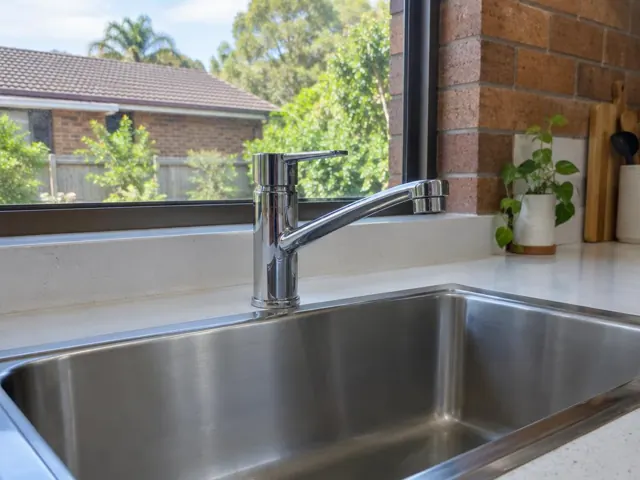 Chrome kitchen mixer tap over a stainless steel sink with stone benchtop and brick wall in Frenchs Forest